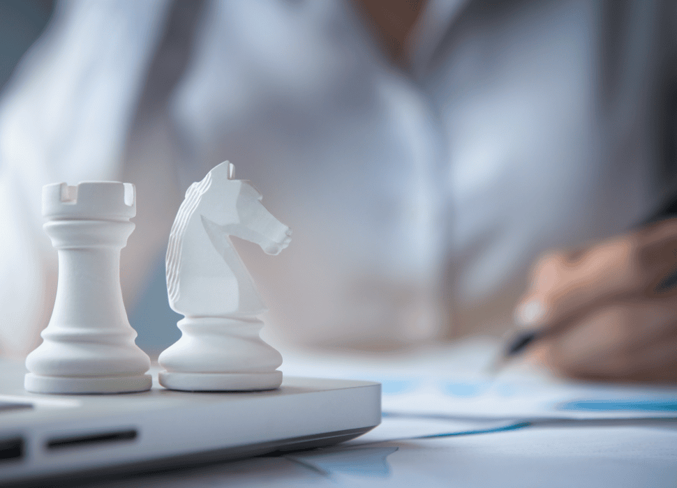 a closeup of a man writing a report and two chess pieces on top of a laptop